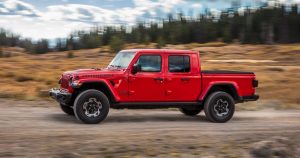 A red 2020 Jeep Gladiator driving on a dirt road with hills and trees in the background